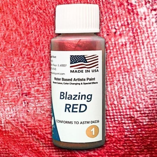 A bottle of Blazing Red water-based artists paint, featuring a textured red background and a label with the American flag, "Made in USA," and compliance with ASTM D4236.