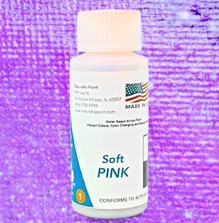 A bottle of water-based artist paint labeled "Soft Pink," set against a textured purple background. The label features a Made in USA flag and the manufacturer details.